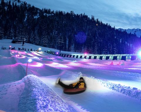 Man slides down the tubing lanes under neon lights. 