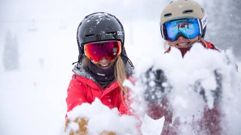 Two girls holding out the new snow and smiling