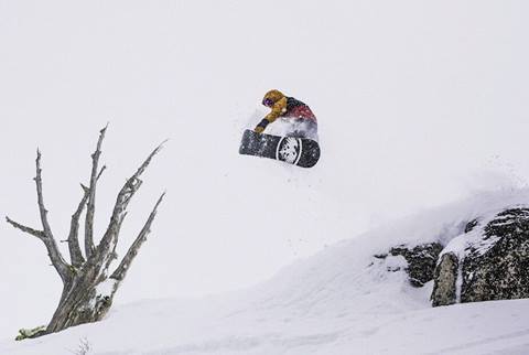 Snowboarder hitting a method grab off of a cliff