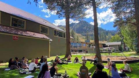 This image shows students sitting in a circle during an outdoor session of Yoga Teacher Training in the Palisades Tahoe base area. 