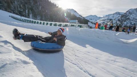 A boy smiles for the camera as he slides down the shoot on a snow tube. 