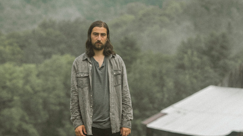 Artist Noah Kahan standing in front of greenery