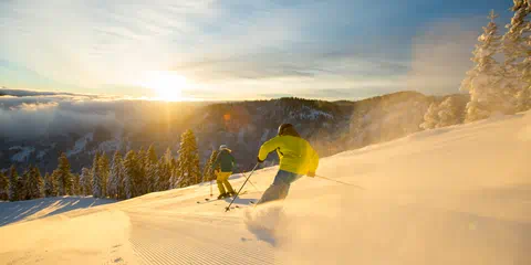 Two skiers on a groomer during sunrise