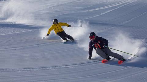 Mountain Sports School instructor skies down a groomer with another skier during a lesson. 