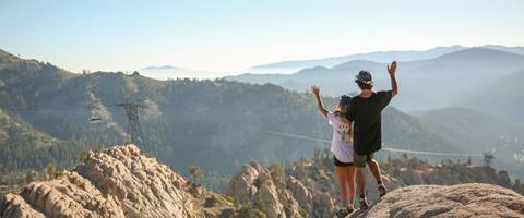 Scenic photo of a couple hiking the tram at Palisades Tahoe and waving into the distance. 