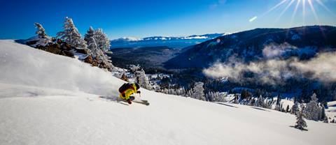 Skier going down a powder slope with Lake Tahoe in the background