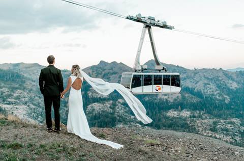 Newlyweds overlook the valley below as a Palisades Tahoe tram drifts past. 