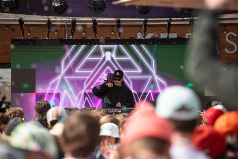 A DJ spins behind a booth as onlookers enjoy.  