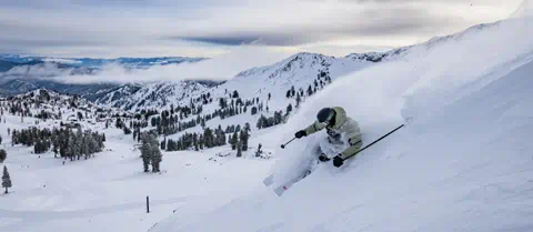 A skier glides through powder on a pair of demo skis with vistas in the background at Palisades Tahoe. 