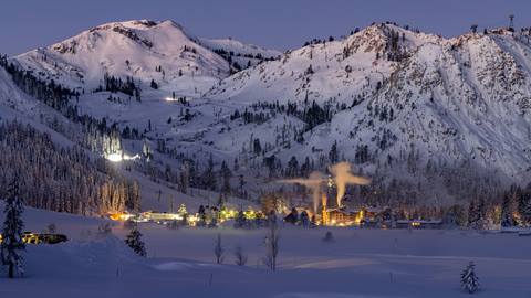 Palisades Tahoe and The Village lit up beneath snowy mountains