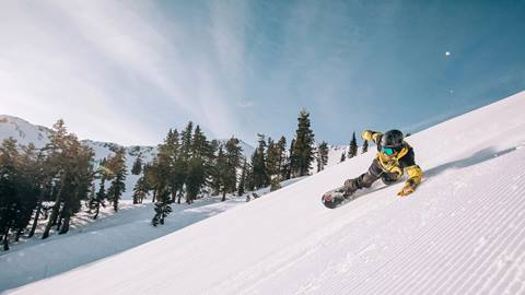 Snowboarder riding corduroy at Palisades Tahoe on a sunny day